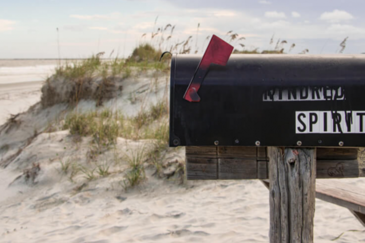 close-up of a mailbox that says "kindred spirit" with the beach in the background