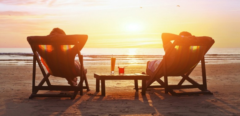 two people sitting in beach chairs watching the sunset | Sunset Vacations